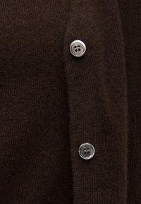 Material tricotat maro închis cu două nasturi bej deschis cu patru găuri, aliniați vertical pe o închidere a unei piese vestimentare.