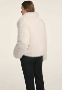 Biała kurtka z sztucznego futra z szerokim kołnierzem i długimi rękawami, charakteryzująca się miękką, puszystą teksturą oraz lekko skróconym krojem.