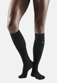 Calzini a compressione neri al ginocchio realizzati in materiale liscio. Presentano una parte superiore a costine e un design semplice con un logo sottile.