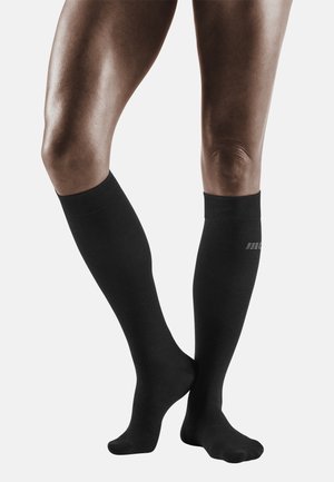 Calzini a compressione neri al ginocchio realizzati in materiale liscio. Presentano una parte superiore a costine e un design semplice con un logo sottile.