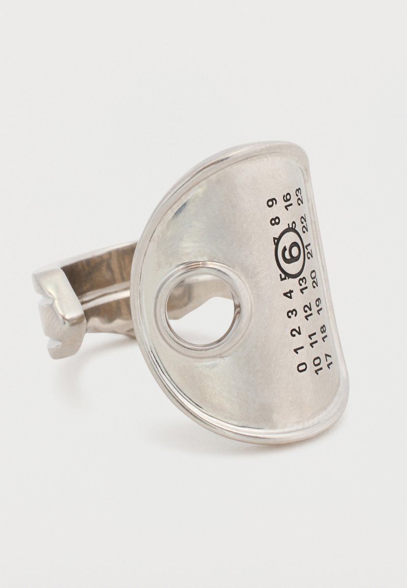 Bague en métal argenté avec un design incurvé, présentant une découpe circulaire et des chiffres imprimés de 0 à 23, avec un cercle noir autour du chiffre 6.