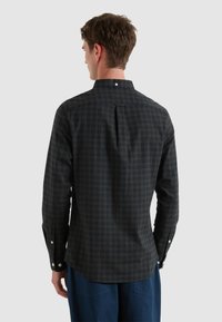 Heren donker geruit overhemd met een button-down kraag, lange mouwen en een rugplooien voor extra comfort. Katoenen stof met subtiele textuur.