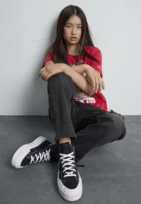 Svarte høye sneakers med hvite snørebånd og gummisåler. Skoene har søm detaljer og en litt overdimensjonert design.