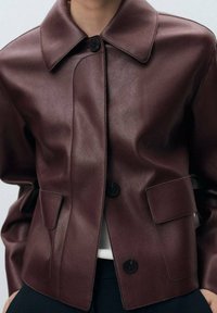 Burgundy leather jacket with a structured collar, button closure, and two front pockets. Smooth texture with a sleek finish.