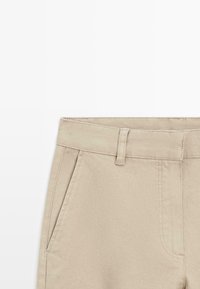 Pantalons en coton beige avec une coupe droite. Présentent une taille plate, des poches latérales et des coutures visibles le long des coutures.