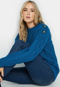 Blaues Kabelstrick-Pullover mit Rundhalsausschnitt, der strukturierte Muster und drei dekorative goldene Knöpfe an der Schulter aufweist.