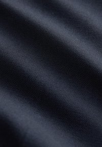Gros plan sur un tissu bleu marine foncé montrant une fine texture tissée et des plis doux créant des ombres douces.