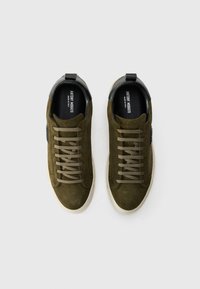 Ein Paar olivgrüne Wildledersneaker mit beigen Schnürsenkeln und weißen Sohlen, von oben auf einem weißen Hintergrund betrachtet.