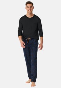 Černé tričko s dlouhým rukávem a přední kapsou, doplněné modrými pyžamovými kalhotami s tmavým abstraktním listovým vzorem a šňůrkou v pase.