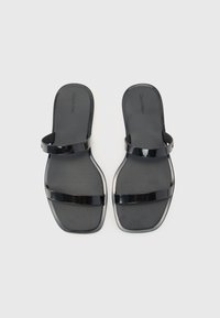 Černé ploché sandály s hladkým povrchem, vybavené dvěma lesklými pásky a minimalistickým designem. Plochá podešev s zaoblenými okraji.