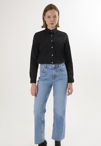 Sort skjorte med knapkrave og hvide knapper, sammen med højdeskårne lys blå jeans. Glat stof, afslappet pasform.