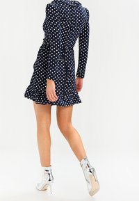 Námořnické šaty s puntíky a dlouhými rukávy, s volánkovým lemem. V kombinaci s lesklými stříbrnými vysokými podpatky na kotníky. Hladká textilní struktura.