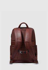 Bruine leren rugzak met gewatteerde, verstelbare riemen, gestructureerde panelen, een bovenhandvat en zijritszakken. Minimalistisch ontwerp.