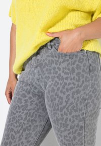 Jeans de mezclilla con estampado de leopardo gris, de diseño ajustado y con una textura sutil. Combinados con un suéter de punto suelto y de color amarillo brillante.