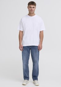 T-shirt en coton blanc à manches courtes, associée à un jean bleu à jambe droite et des baskets blanches. Design simple et décontracté sans motifs visibles.