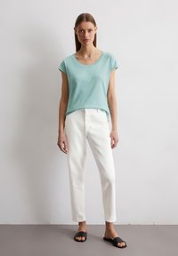 Lichtblauw shirt met korte mouwen, witte broek en zwarte slippers. Zacht materiaal, relaxte pasvorm, ronde halslijn, minimalistisch ontwerp.