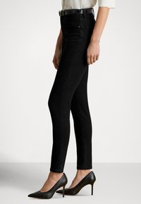 Sorte skinny jeans laget av denim, med høy midje og frontlommer. Brukt med spisse svarte hæler og en hvit bluse.