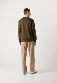 Sweatshirt vert olive à col rond et à poignets côtelés, associé à un pantalon beige clair ; les deux présentés de dos sur un fond neutre.