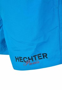 Un short de bain bleu vif en matériau léger présente un logo noir "HECHTER" et un accent rouge "Paris" près de l'ourlet.