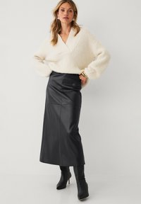 Strikket creme farvet sweater med V-hals, parret med en sort læder midi-nederdel. Modellen har sorte ankelstøvler på. Glatte teksturer og kontrasterende farver.