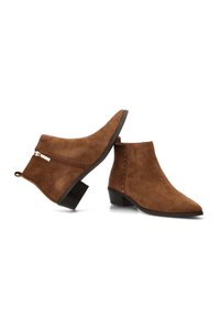 Botas de ante marrón hasta el tobillo con punta afilada, tacón bajo en bloque, cierre de cremallera lateral y tachuelas decorativas a lo largo de la costura exterior.