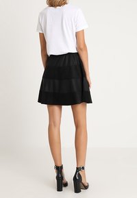 Svart lagerkjol i mjukt tyg med en texturerad design. Kombinerad med en enkel vit t-shirt och svarta högklackade skor.