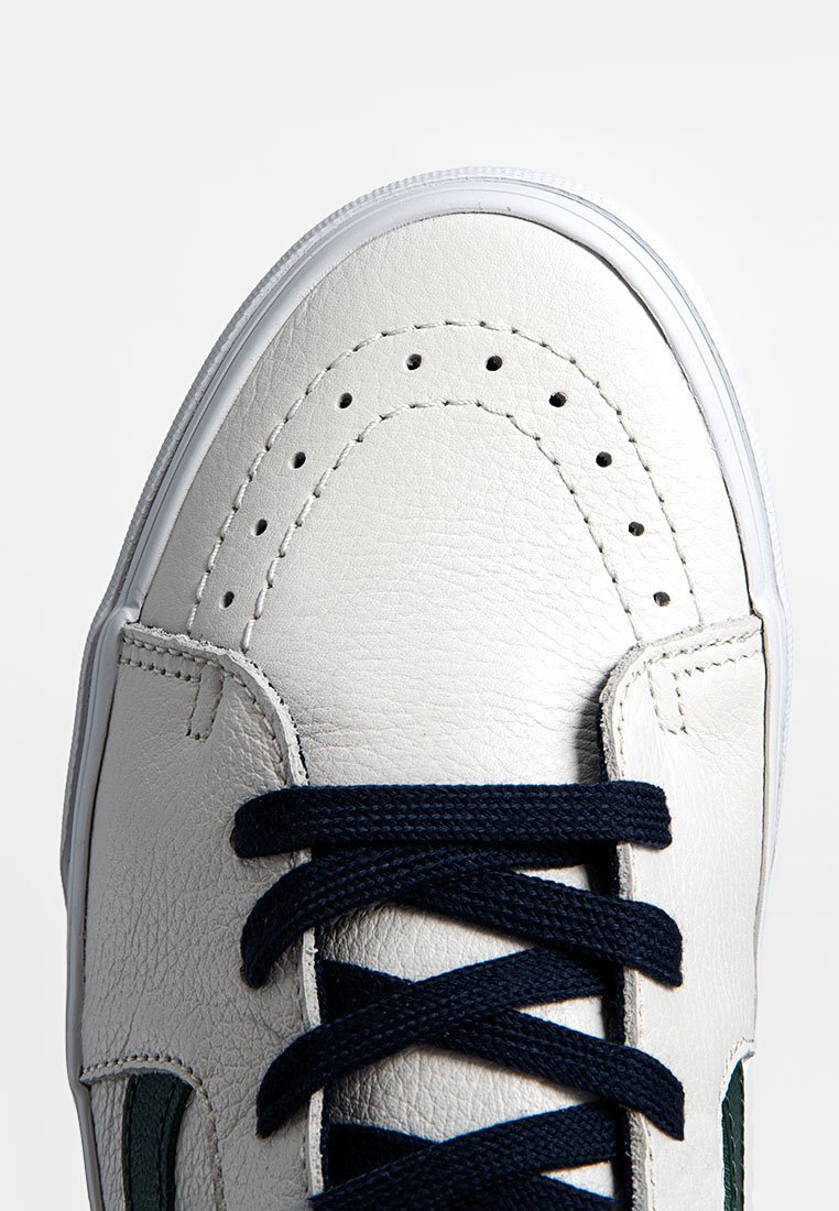 Weiße Leder-Sneaker mit runder Zehenform, marineblauen Schnürsenkeln, perforierten Details und grünen Akzenten an den Seiten. Strukturierte Oberfläche.