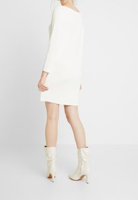Abito in maglia a coste color crema con scollatura ampia e maniche lunghe, abbinato a stivali bianchi aderenti fino al ginocchio con zip.
