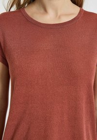 Top rosso a maniche corte realizzato in tessuto testurizzato con scollatura rotonda. Il materiale presenta una leggera lucentezza e accenti più chiari.