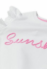Bílá košile s krátkým rukávem, na které je vyšitý růžový text "Sun" a krajkové detaily na ramenou. Hladká textura a jednoduchý design.