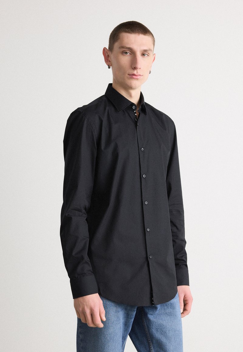 Svart langermet skjorte med krage-design, med en knappestolpe og svarte knapper. Glatt stoff, satt sammen med blå jeans.