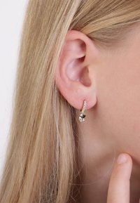 Goudkleurige oorbellen met een enkele heldere edelsteen en een kleinere, donkere edelsteen, gezet in een gebogen ontwerp met micro-pavé accenten.