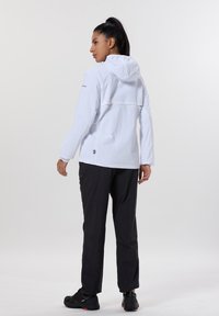 Valkoinen kevyt takki, jossa huppu ja selkäosa, yhdistettynä mustiin housuihin ja mustiin kenkiin. Yhteensä sileä rakenne.