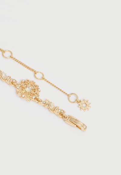 Βραχιόλι σε χρυσό τόνο με διαφανή κρυσταλλική ανθική διακόσμηση και ρυθμιζόμενη αλυσίδα που φέρει ένα μικρό γοητευτικό μοτίβο σε σχήμα μικρού αστεριού σε λευκό φόντο.