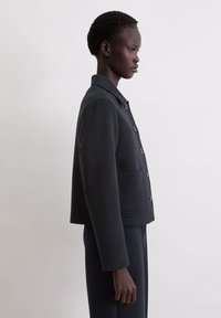 Czarna krótka kurtka z kołnierzem, zapinana na guziki z bocznymi kieszeniami. Miękka w dotyku, o strukturalnym kroju; dopasowany fason.