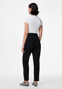 Calças pretas sob medida com cintura alta e corte justo, combinadas com um top branco ajustado. Os sapatos apresentam um padrão de zebra preto e branco.