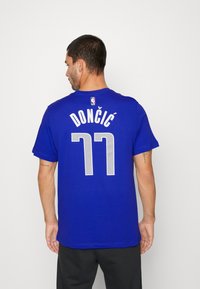 Kongelig blå trøye med korte ermer. Har "DONČIĆ" og nummer "77" i hvit skrift. Laget av mykt, glatt stoff.