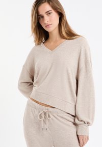 Jasnobeżowy sweter z dekoltem w serek o luźnym kroju, szerokich rękawach i miękkiej fakturze, w połączeniu z pasującymi spodniami dresowymi z troczkiem w talii.