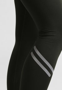 Svarta sportleggings gjorda av stretchigt tyg, med en slät yta och två grå ränder som accentuerar lårområdet.