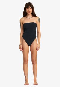 Costume da bagno intero nero senza spalline con design testurizzato, aperture per le gambe a taglio alto e copertura minimale. Tessuto morbido senza decorazioni.
