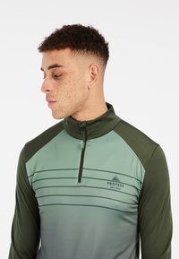Groene sportieve half-zip top met een gradient ontwerp, contrasterende donkergroene mouwen, horizontale strepen en een logo op de borst.