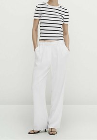 Gestreept cropped T-shirt in wit en zwart katoen met korte mouwen, gecombineerd met luchtige witte broeken van stof, voorzien van zijzakken.