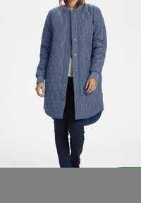 Gep quiltete blaue Jacke mit Rundhalsausschnitt, Druckknöpfen, langen Ärmeln und einem längeren Rückensaum. Sie hat eine glatte, leichte Textur.