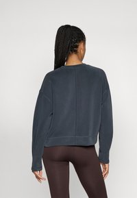 Felpa in cotone blu scuro con vestibilità comoda, spalle ribassate e maniche a costine, abbinata a leggings marroni a costine.