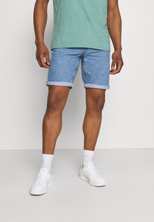 Shorts in denim con risvolti, di colore azzurro chiaro e vestibilità rilassata, abbinati a una maglietta verde e sneaker bianche.