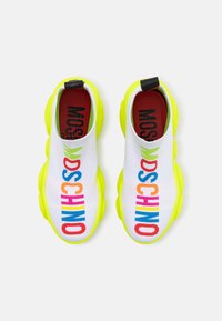Bílé plátěné tenisky na klouzání s jasně žlutými podrážkami, které mají barevný nápis "MOSCHINO" přes vrchní část. Texturovaný pletený materiál, kulatý tvar špičky.
