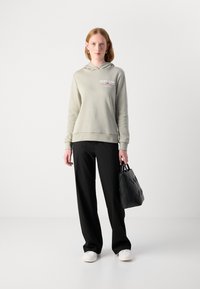 Sudadera gris claro con el logo "GANT 1949", pantalones negros de pierna ancha y un bolso negro elegante con un patrón en zigzag. Zapatillas blancas.