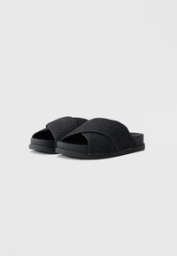 Sandales en denim noir à bout ouvert avec un design croisé sur le dessus. Présente une surface texturée et une semelle plate noire.