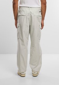 Pantaloni cargo grigio chiaro con vestibilità rilassata, caratterizzati da molteplici tasche laterali e un tessuto testurizzato. Completati con sneaker beige.