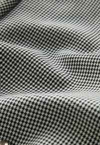 Tissu à motif pied-de-poule noir et blanc avec des plis visibles et une surface texturée.